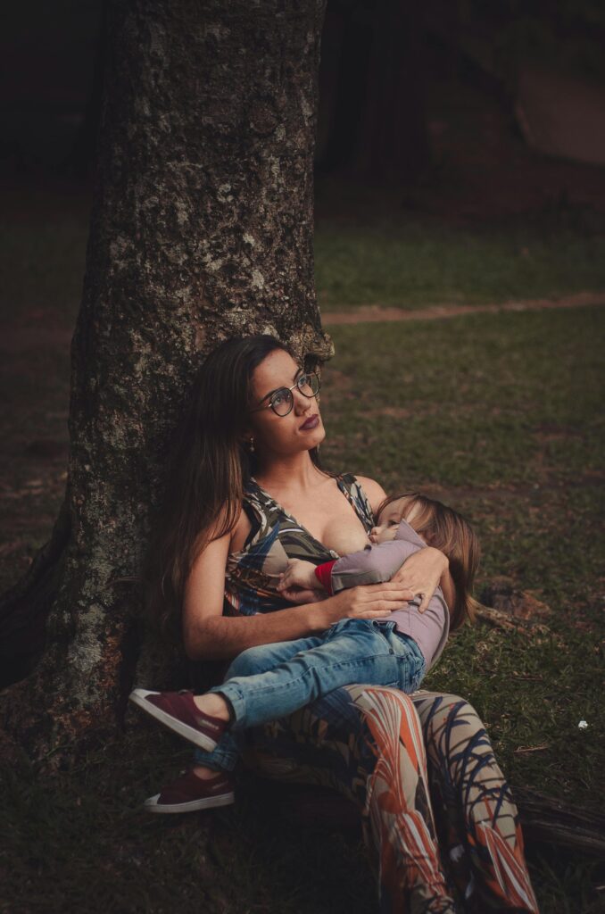 A mother lovingly embraces her child while sitting under a tree outdoors.